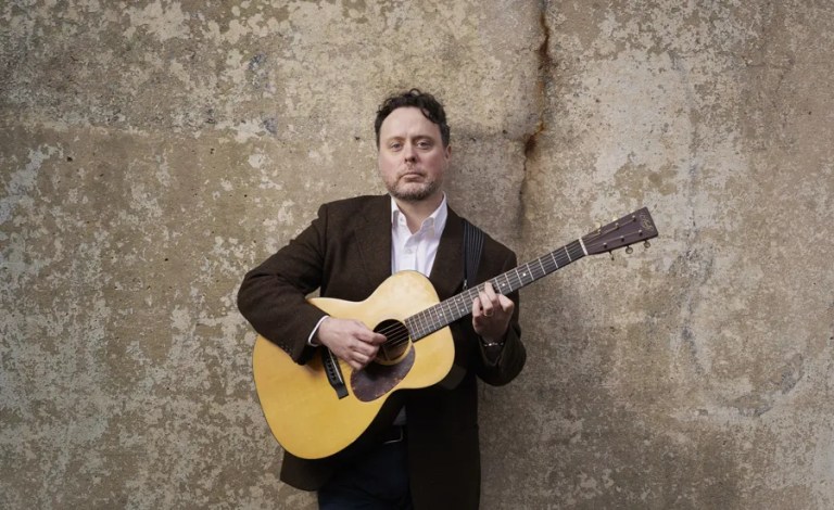 Guitarist Grant Gordy standing holding an acoustic guitar