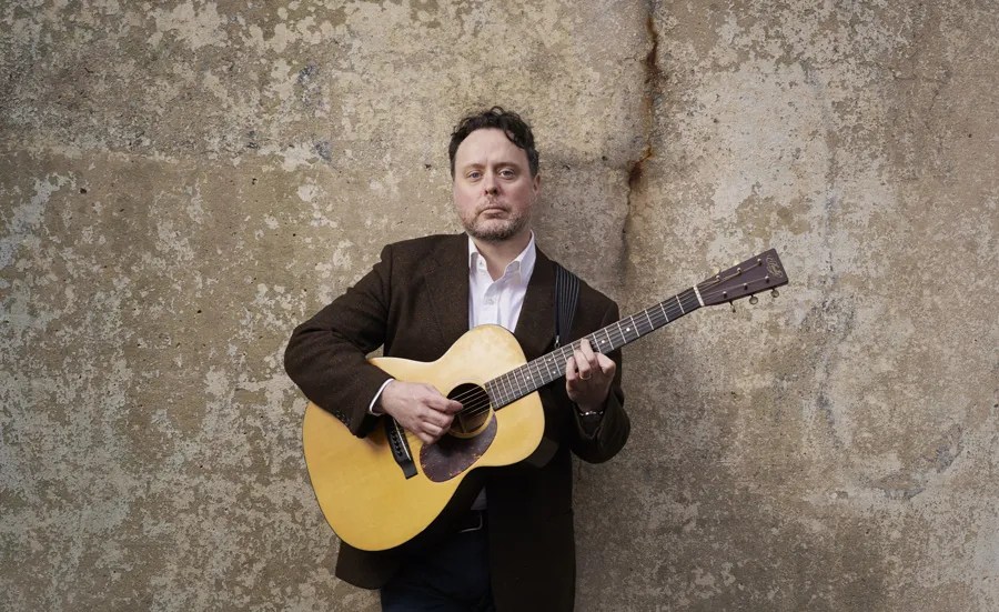 Guitarist Grant Gordy standing holding an acoustic guitar