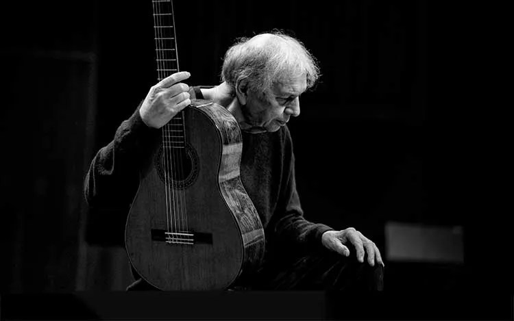 Ralph Towner seated, holding a an acoustic guitar.