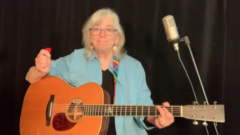 Cathy Fink seated in front of a microphone holding a guitar