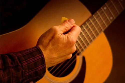 closeup of a guitarist strumming an acoustic guitar