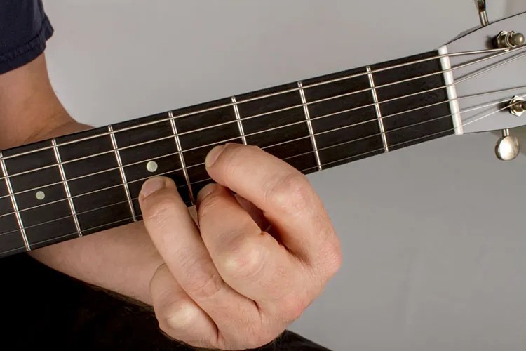 A guitarist frets a D-chord shape at the fourth fret