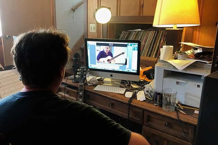 guitar teacher giving online lesson in front of a computer