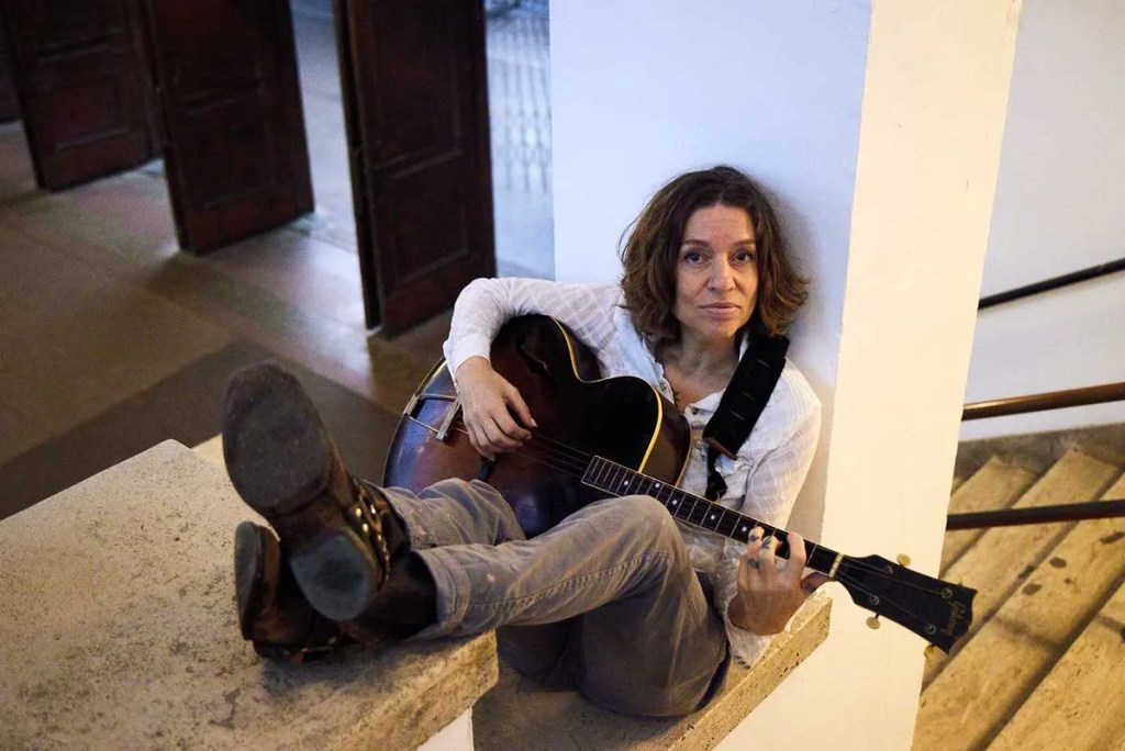 Ani DiFranco seated on a stairway playing an archtop guitar. Photo by Danny Clinch