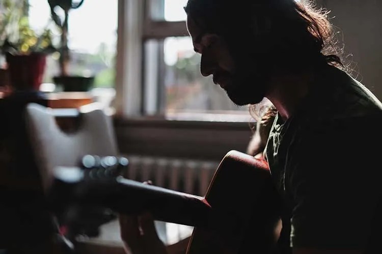 a person sitting down playing acoustic guitar