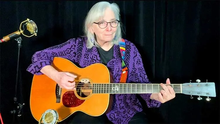 Cathy Fink, seated with guitar, teaches a guitar lesson on boom-chuck accompaniment patterns