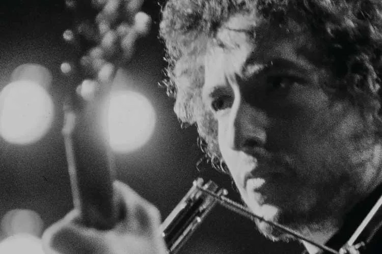 Bob Dylan holds a guitar in a promotional photo from Columbia Records