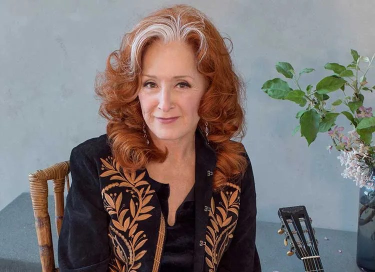 Bonnie Raitt seated and wearing a black jacket with gold embellishments