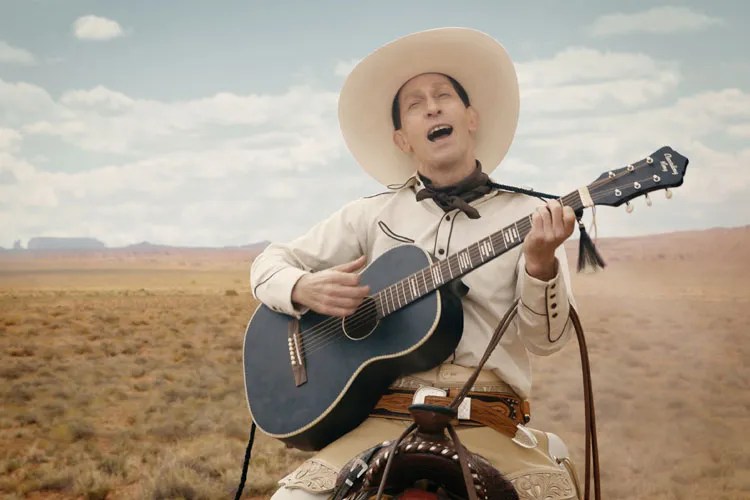 Buster-Scruggs-playing-guitar-and singing-while-riding a horse