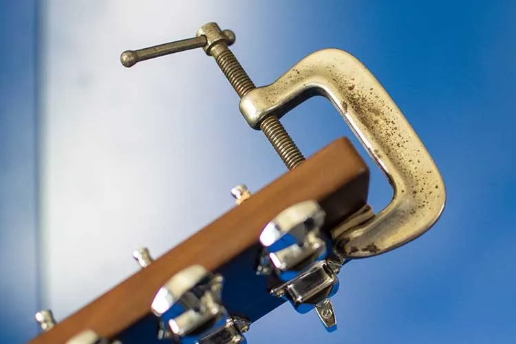 closeup of a guitar headstock with a c-clamp attached to it