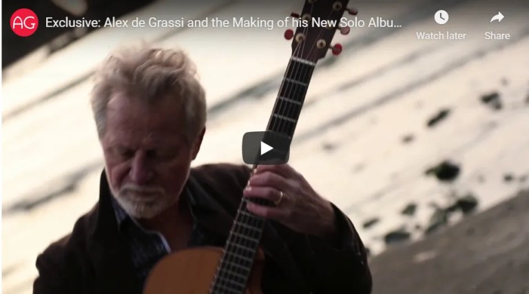 Alex De Grassi playing acoustic guitar on a rocky beach