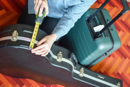 Measuring a a guitar case with a tape measure, with suitcase in background.