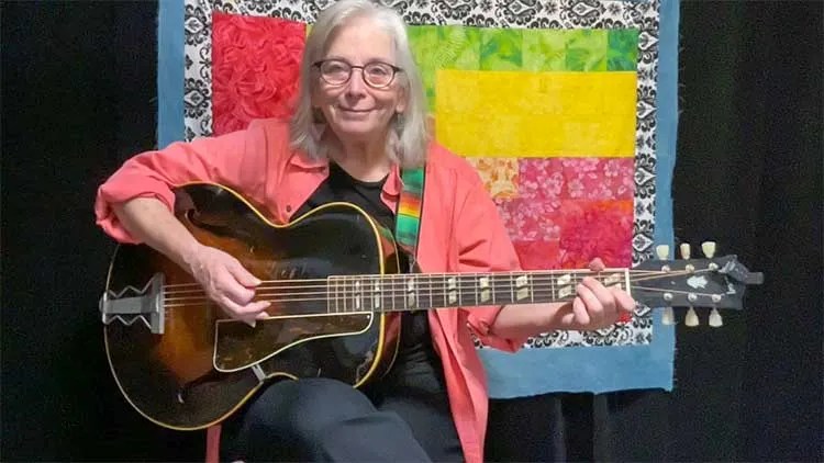 Cathy Fink, seated with guitar, teaching a lesson on strumming