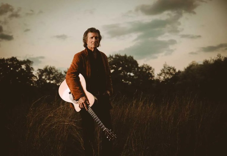 Chris-Smither-standing-in-field-with-acoustic-guitar-photo-Jo-Chattman-4