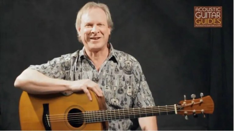 Danny Carnahan smiling with his acoustic guitar resting across his lap