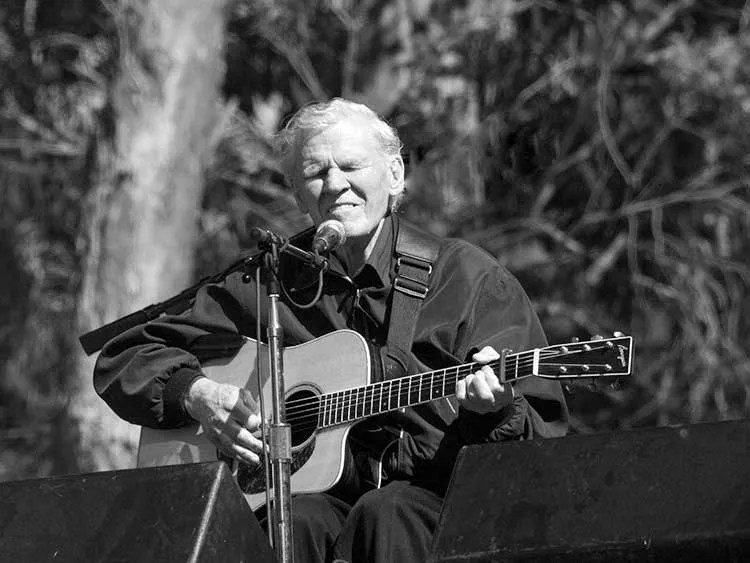 Doc Watson playing guitar onstage. Photo by Eric Frommer