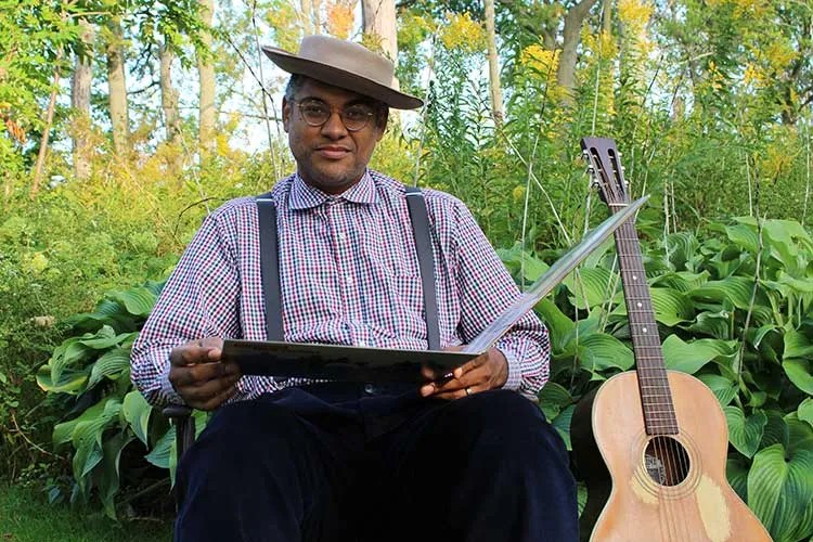 Dom Flemons seated with acoustic instruments. Photo by Nate Kinard Jr.