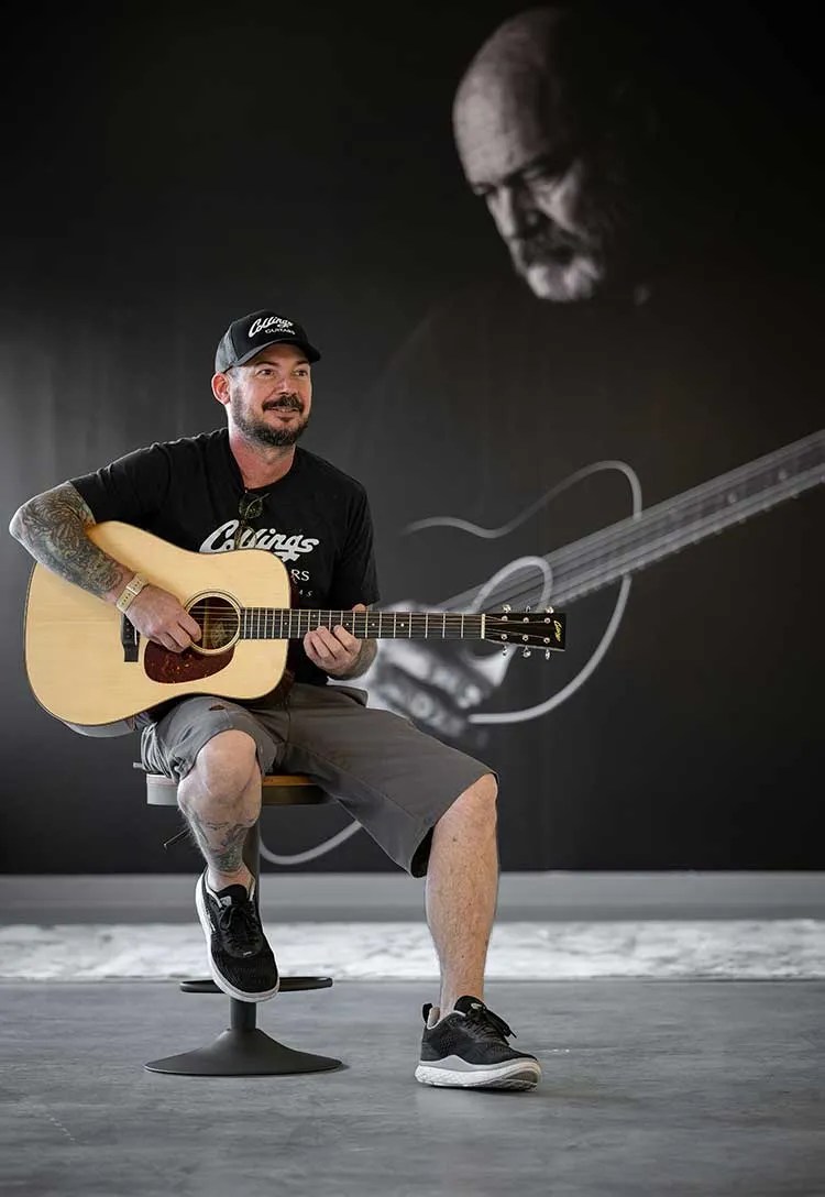 Steve Nall seated with guitar in front of a BIll Collings backdrop photo