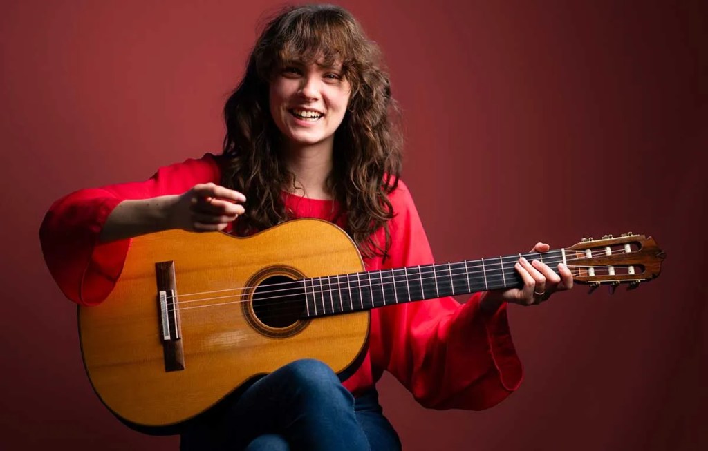 Laura Snowden smiling (and pointing at camera) with guitar.