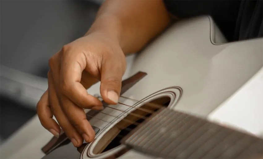 close up of hand picking strings over the soundhole of an acoustic guitar