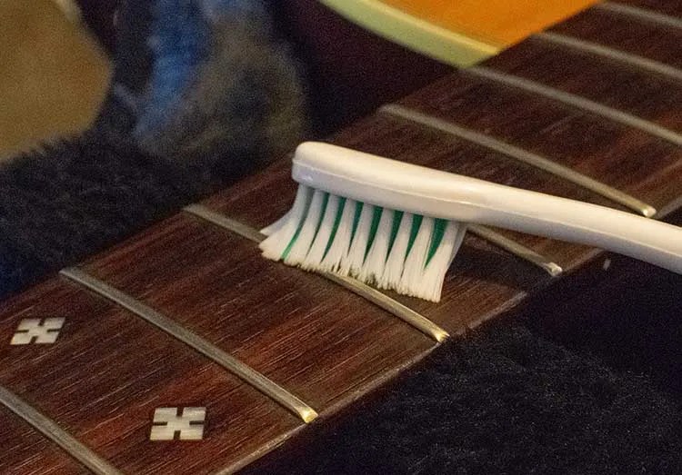 a toothbrush being used to clean a guitar fretboard