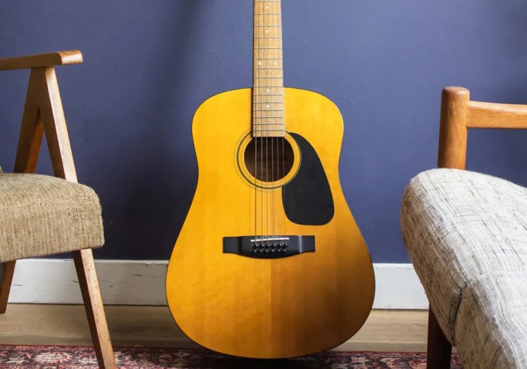 acoustic guitar on a stand in front of a blue backdrop