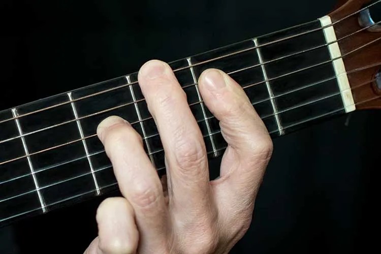 close up photograph showing three fingers on a guitar neck playing a Gmaj9 chord