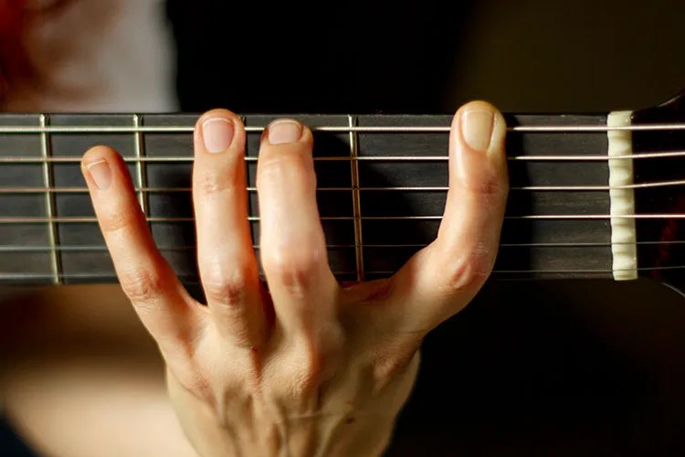 Woman's hand on acoustic guitar fretboard