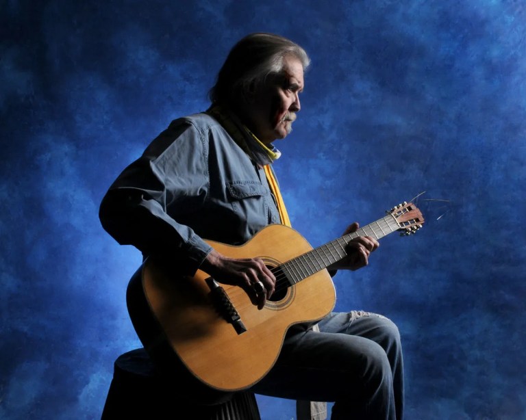 Guy Clack sits on a chair with his guitar