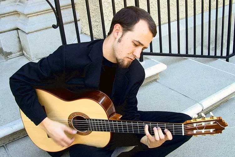 Gyan Riley seated on steps with a nylon-string guitar photo by Robin Hanleyi