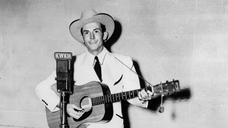 Hank Williams holding guitar in front of radio microphone