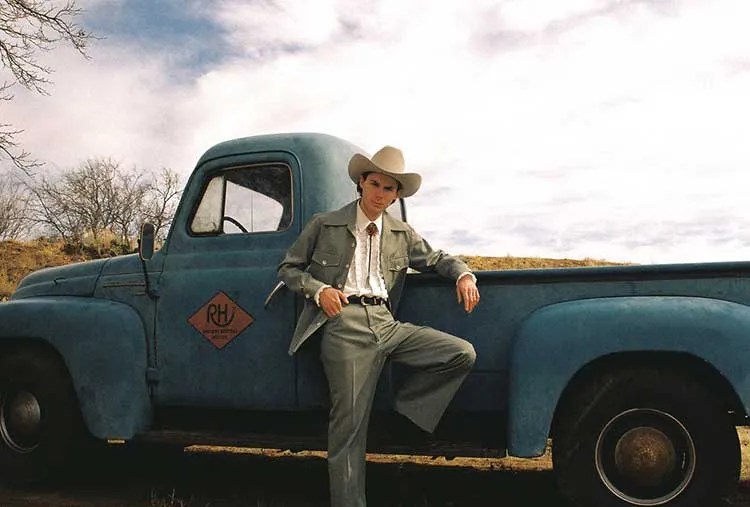 Hayden Pedigo, in cowboy hat, standing beside a vintage pickup truck