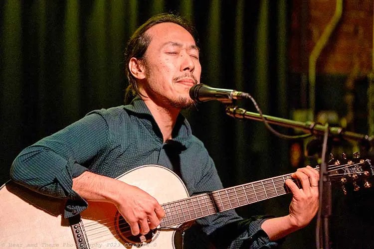 Hiroya Tsukamoto playing acoustic guitar and singing onstage