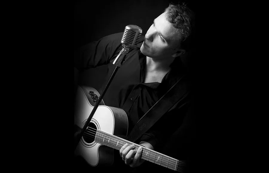 man-singing-into-vintage-microphone-while-playing-acoustic-guitar