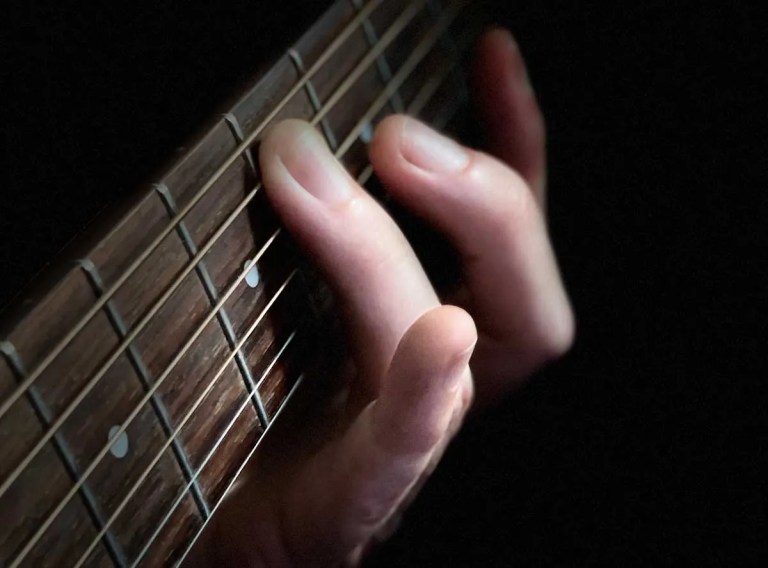 closeup of hand fretting strings on an acoustic guitar