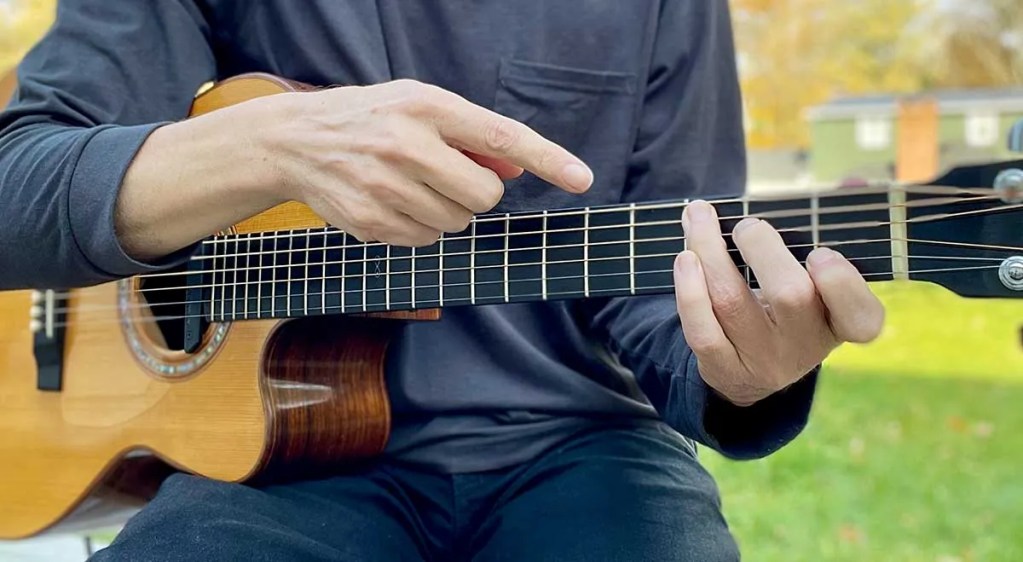 Close up of an acoustic guitarist with finger pointing at fretboard