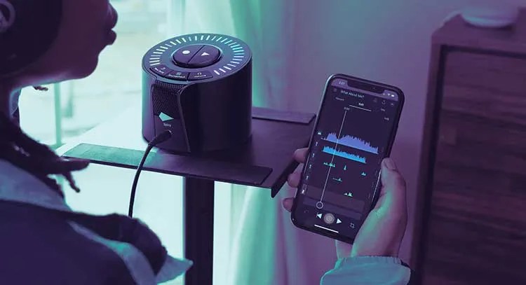 action shot of a vocalist singing into the iZotope Spire Studio unit while holding a smartphone and using the izotope spire studio app