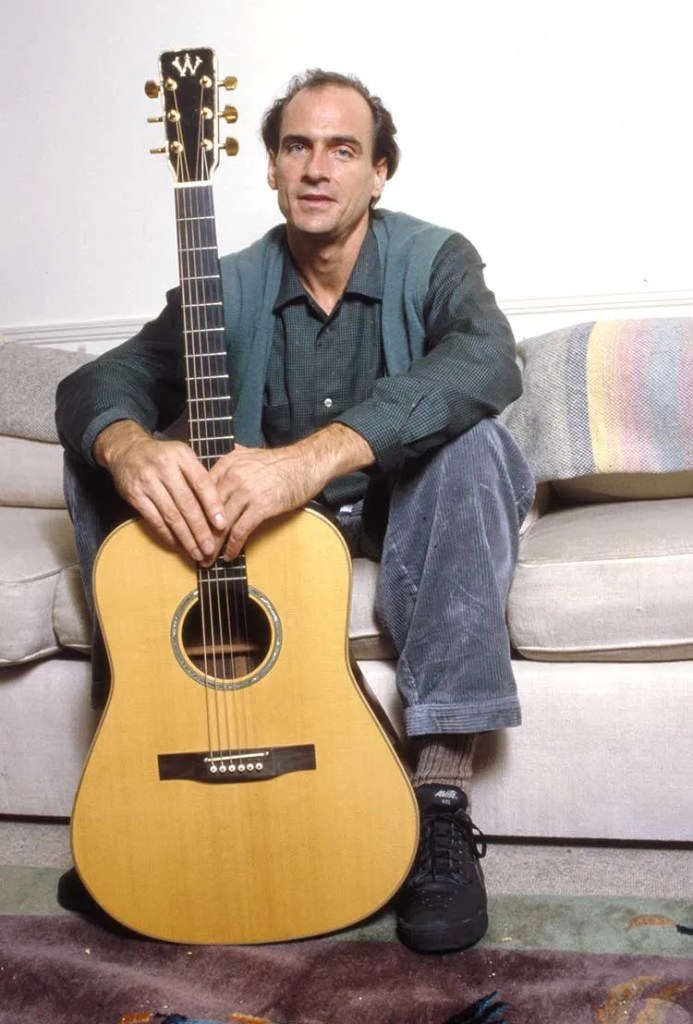 James Taylor sitting on couch with acoustic guitar