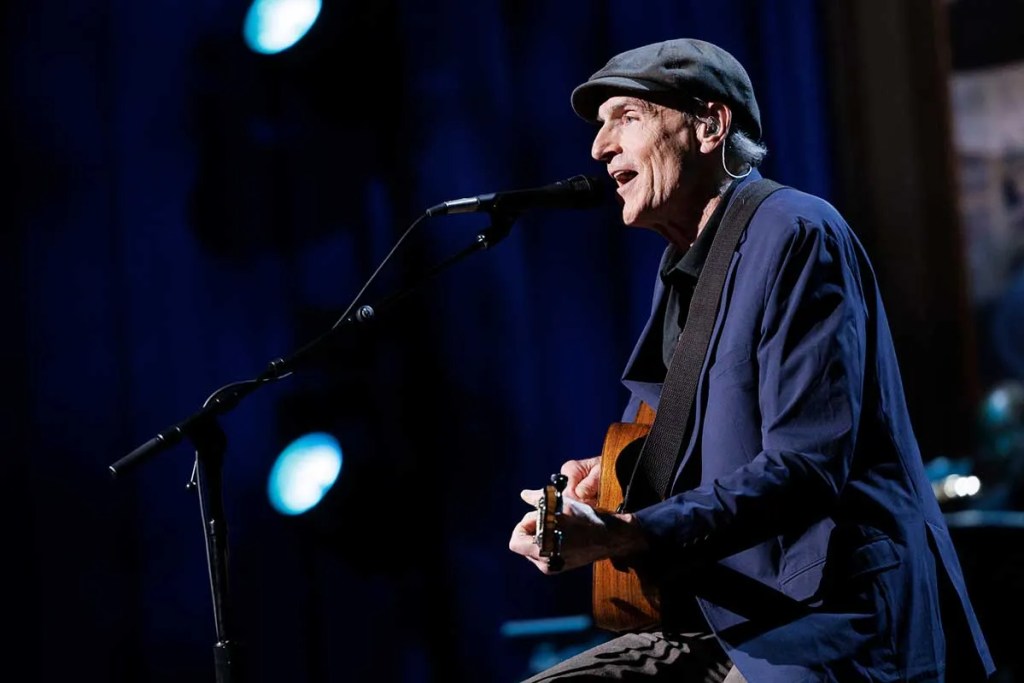 James Taylor playing guitar and singing onstage