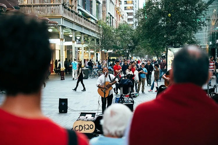 busking guitarist in the street with a PA and a sign that says CD $20