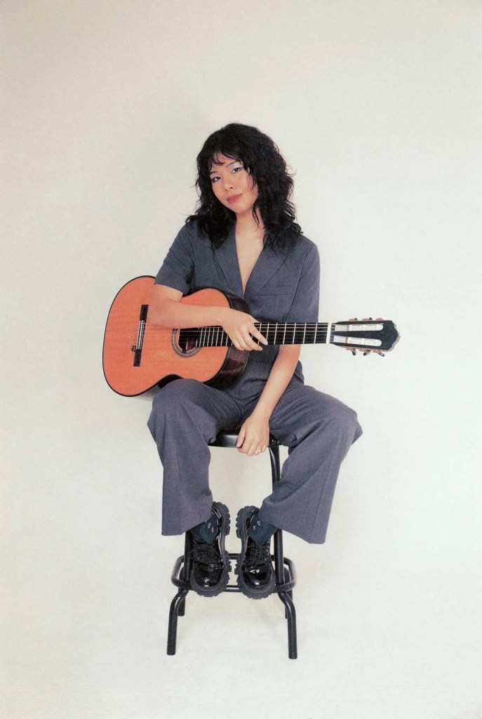 JiJi seated on a stool with classical guitar. Photo by Kim Cheonga 