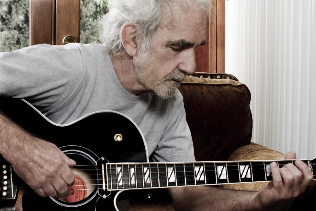 J.J. Cale plays an acoustic guitar.