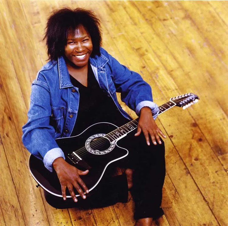 Joan Armatrading sitting on floor with acoustic guitar