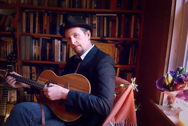 guitarist john doyle sitting in a chair in home library with guitar