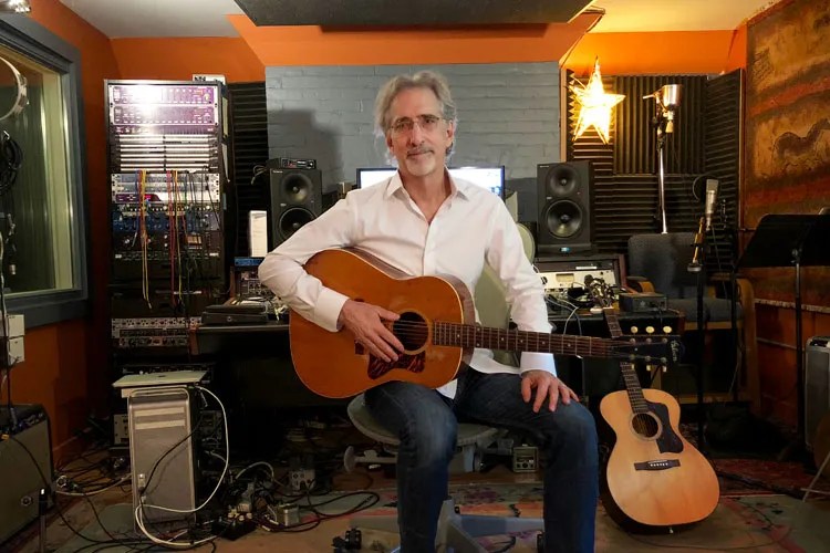 John Leventhal poses in a chair with his guitar