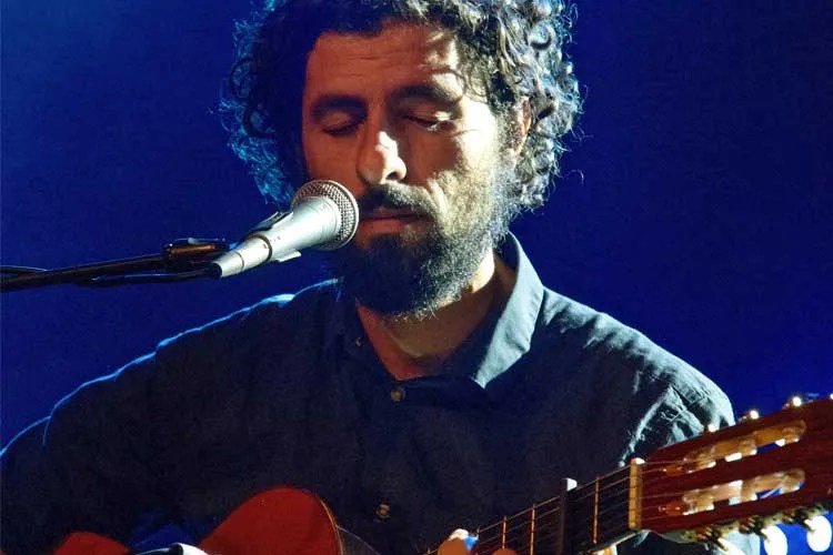 singer-songwriter José González sings into a microphone while holding an acoustic guitar