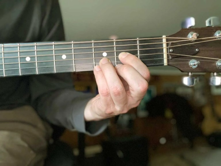 A guitarist's hand fretting a D sus chord.