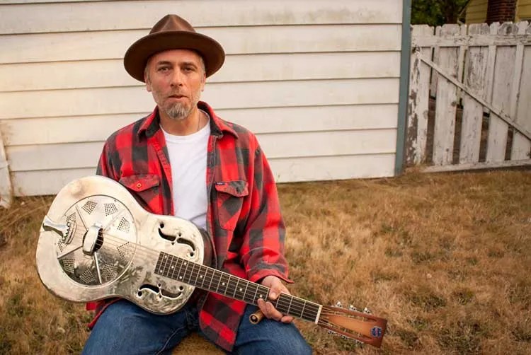 Kelly Joe Phelps sitting outside with his resonator guitar