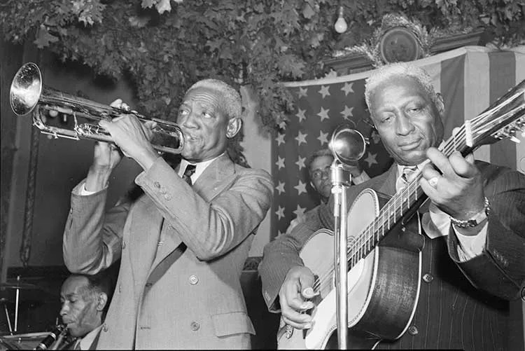 Lead Belly playing guitar onstage with trumpet player