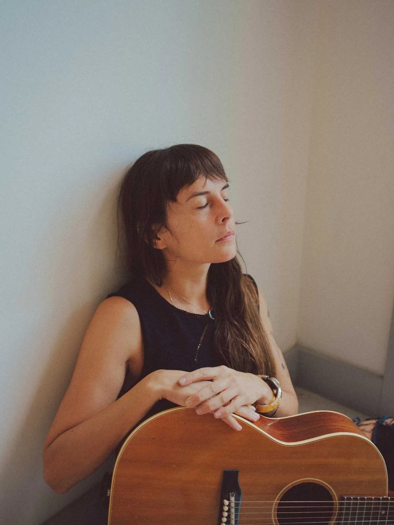 Madi Diaz, eyes closed, rests her arms on an acoustic guitar.